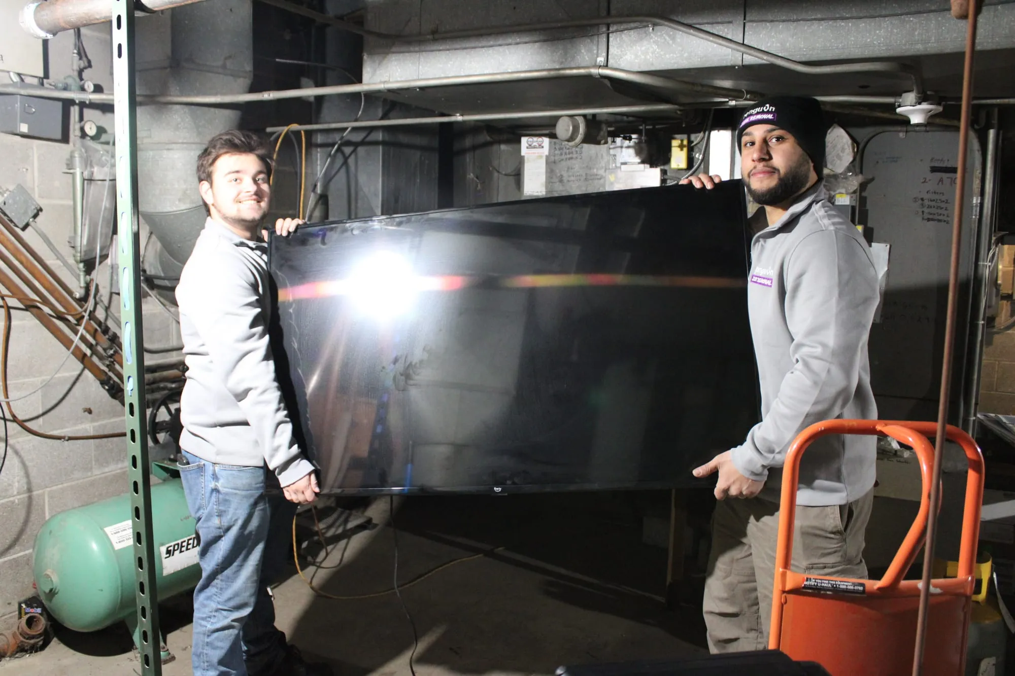 Penguin Junk Removal crew carrying a large flat-screen TV out of a customer's basement