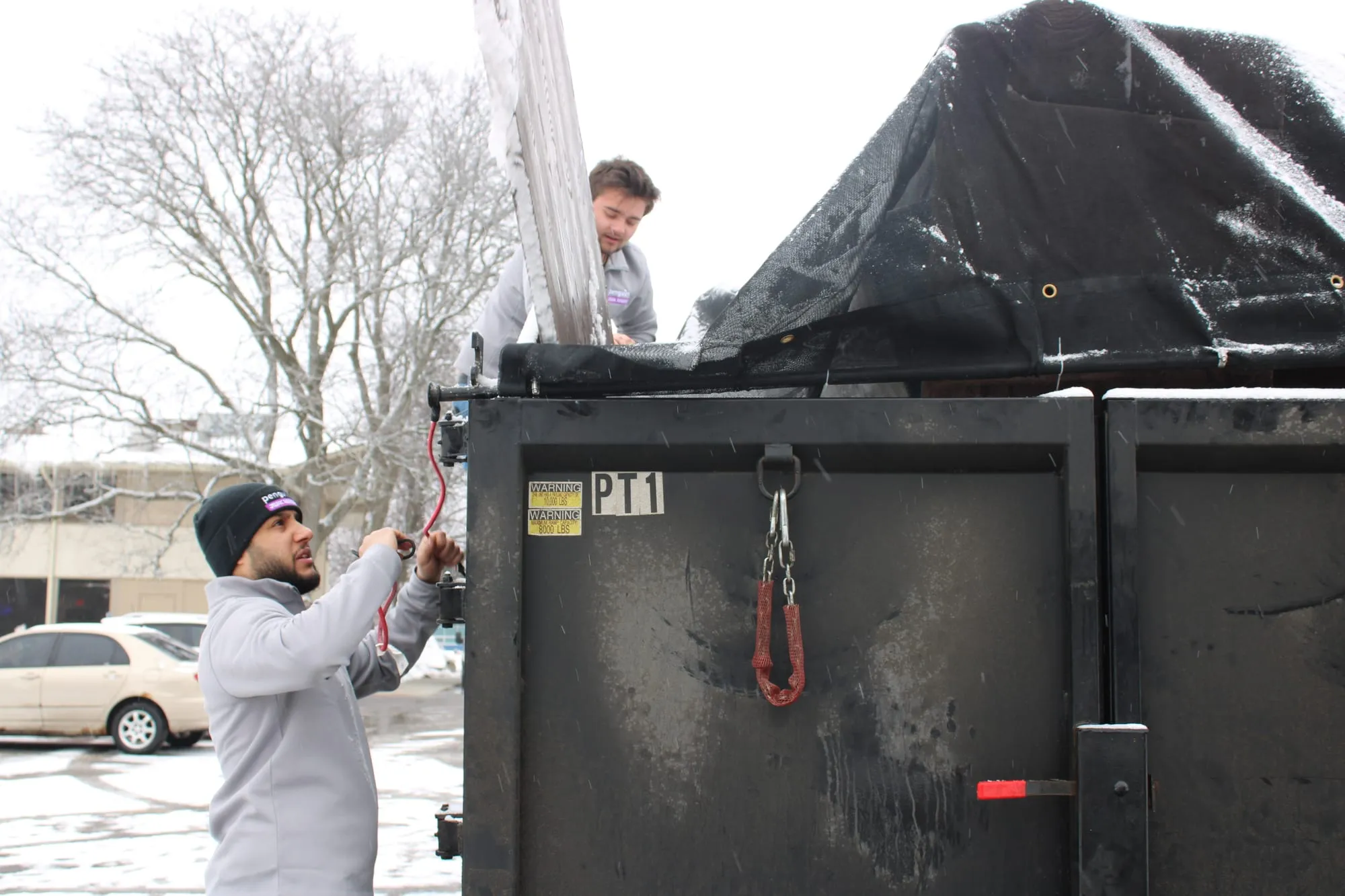 Penguin Junk Removal crew pulling a tarp over a loaded dump trailer