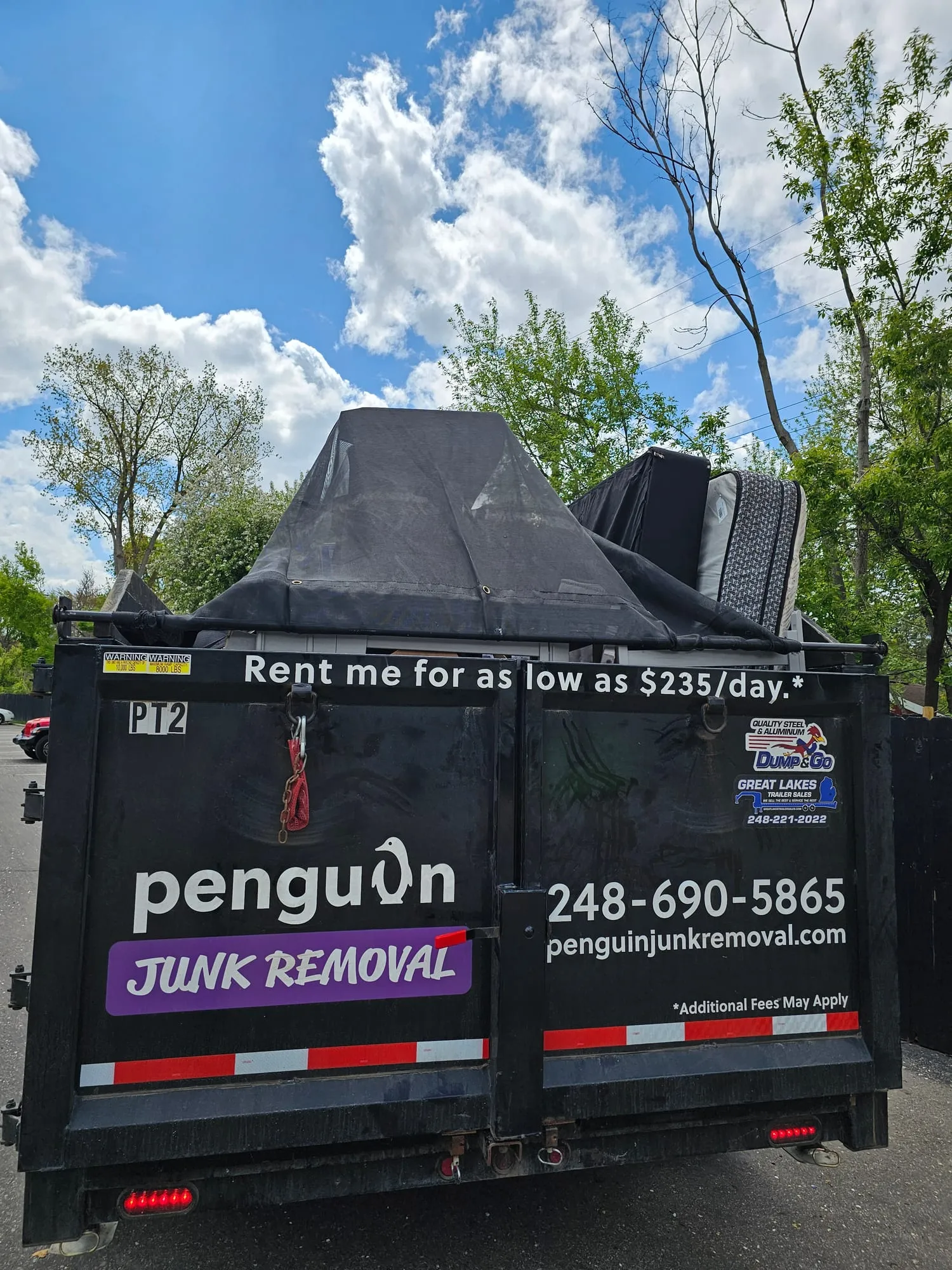 Penguin Junk Removal dump trailer, tarped and branded with the company logo and phone number, parked on a Metro Detroit driveway